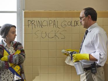 egy nő és egy férfi sárga gumikesztyűben, takarítás közben beszélget az összefirkált fal előtt