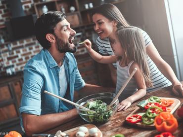 Család az asztalnál, kislány salátát ad az apja szájába