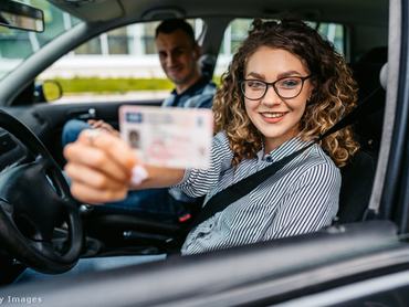 az autóban egy férfi és egy nő ül, a nő az ablakon kerezstül mutatja a jogosítványát