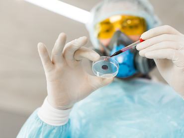 Alulnézetből egy kutató látható egy laboratóriumban, amint vérmintát csepegtet egy Petri-csészébe. Vakcina létrehozásának koncepciója.