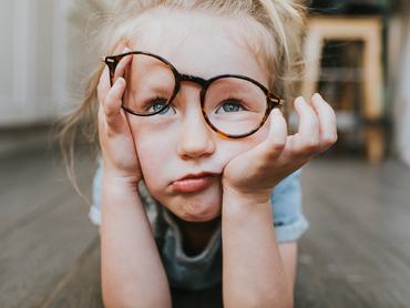 Cute young girl wearing big glasses, looks fed up as she rests her head on her hand. Conceptual with space for copy.