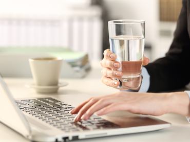 Az irodában a laptop fölött vizet iszik egy nő a kávé után