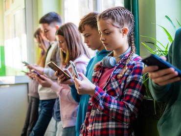 Egymás mellett álló gyerekek telefonoznak az iskola folyosóján
