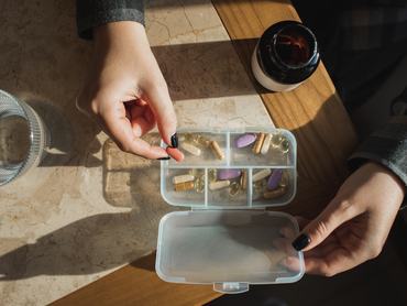 Női kéz kapszulákat rendez egy vitamintartóban