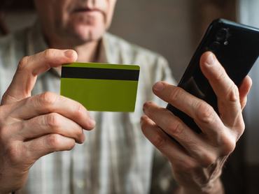 Idős férfi a bankkártyáját és a okostelefonját tartja a kezében az otthonában