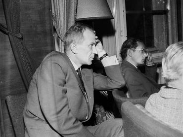 Berkesi András író könyököl egy székre, az előtte lévő sorban egy szemüveges és egy szőke férfi ül