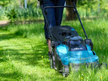 Egy nő fűnyíróval vágja a füvet a kertben.