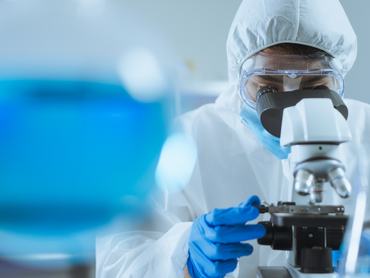 Egy fiatal ázsiai tudós a laboratóriumban beállítja a fókuszt, és mikroszkóppal vizsgálja a sejtek biokémiai szerkezetét. Orvosok és tudósok dolgoznak a koronavírus-járvány idején a laboratóriumban – a COVID-19 témájában