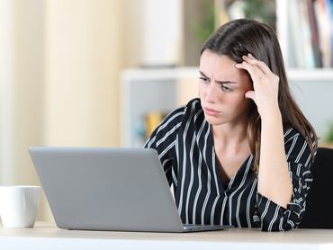 Egy nő aggódó arccal nézi a laptop monitorát az otthonában