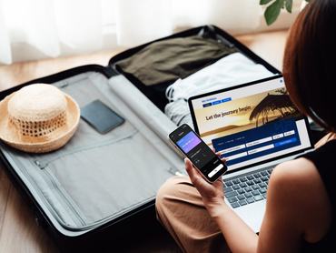Fiatal nő, aki laptopjával és okostelefonjával online foglal repülőjegyet és szállást. Üzleti és szabadidős utazás.