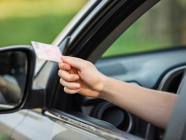 Közelkép egy személyről, aki az autó ablakán kinyújtja a kezét, és a jogosítványát mutatja a rendőrnek ellenőrzés céljából
