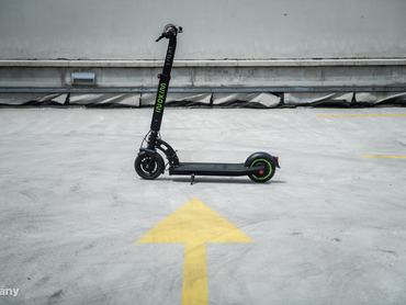 egy elektromos roller áll egy nyíl alakuú, sárga felfestés előtt a betonon