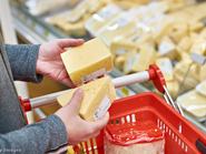 sajtokat néz egy ember a boltban, csak a keze látszik a képen és a sajtos pult