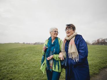 Two senior female friends walking in the park together, laughing and smiling.