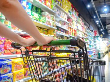 Egy nő bevásárlókocsit tol, és a termékek között válogat egy szupermarketben.