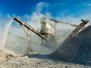 Kőtörő gépek bányában, mellette zúzott kő, homok és kavics.