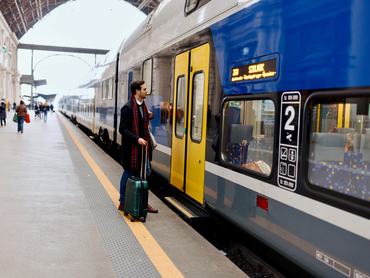 Egy férfi bőrönddel készül felszállni a vonatra egy vasúti pályaudvaron