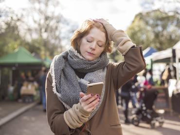 Egy vörös hajú nő egy londoni utcai piacon áll, és szomorúan bámulja az okostelefonját