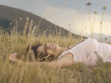 Egy fiatal nő a réten fekszik a fűszálak és virágok között