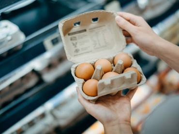 Egy nő egy kinyitott, hat tojást tartalmazó tojástartót tart a kezében a szupermarketben