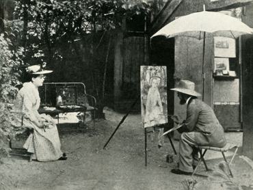 Jobb oldalon, a napernyő alatt Henri de Toulouse-Lautrec ülő helyzetben, egy félkész portré előtt. A bal oldalon a modell, fehér ruhában és kalapban